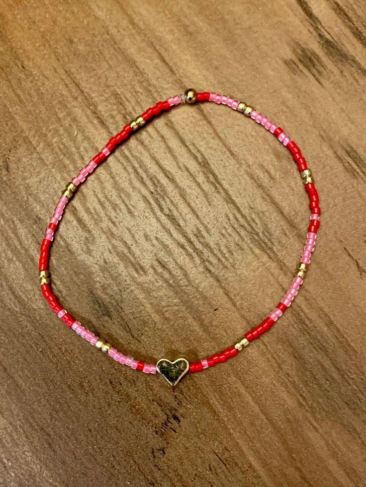 a red and pink bracelet with a heart charm on top of a wooden table next to a