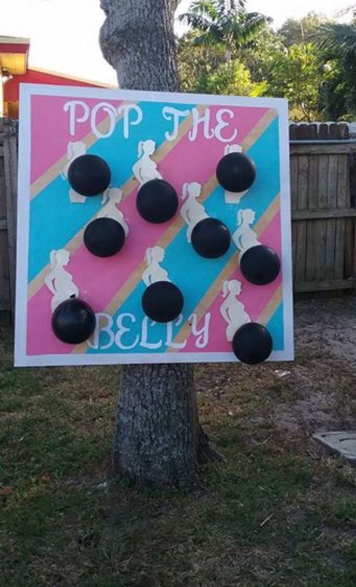 a sign that is on the side of a tree in front of a fence with black balls