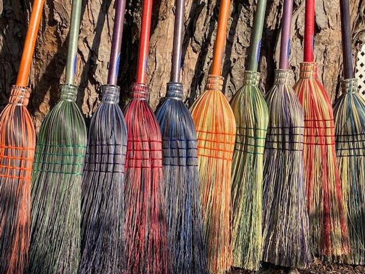 several colorful brooms lined up in front of a stone wall with grass growing on it