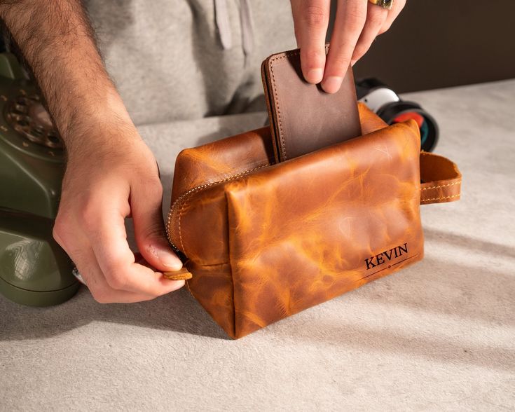 Leather Dopp Kit and Personalized Bag Product Description: Introducing our handcrafted Leather Dopp Kit and Personalized Bag, a perfect blend of style and practicality for your travel and daily needs. Made from premium leather, this bag is designed to keep your essentials organized while adding a touch of sophistication to your accessories. Whether you're on the go or looking for a stylish way to store your toiletries, our Leather Dopp Kit is the ideal choice for those who appreciate quality and Brown Rectangular Pouch With Smooth Grain, Father's Day Rectangular Wallets, Father's Day Everyday Wallets, Travel Bag Organizer, Leather Dopp Kit, Mens Toiletry Bag, Travel Bag Organization, Groomsmen Gifts, Dopp Kit