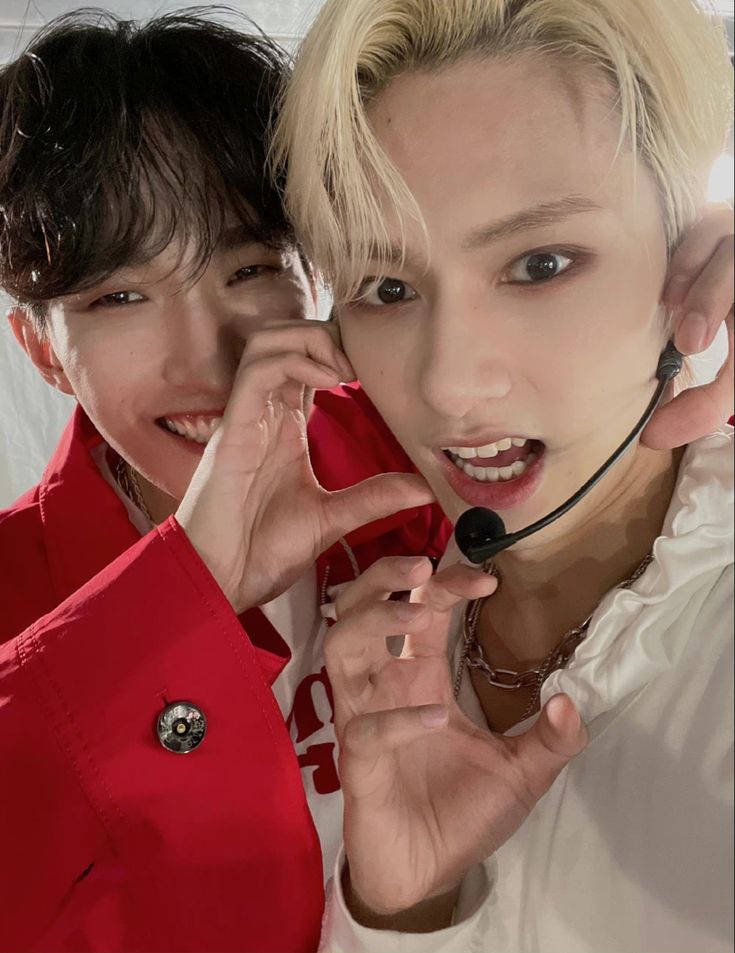 two young men with headsets on posing for a photo together, one is talking on the phone and the other is wearing a red shirt