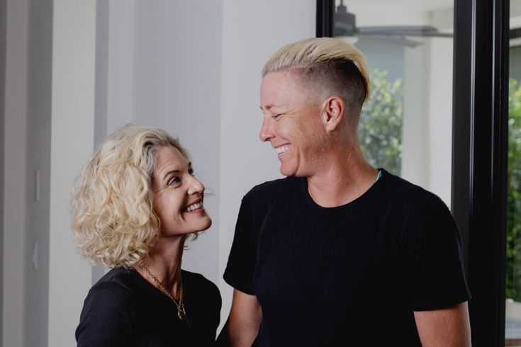 a man and woman standing next to each other in front of a window looking into each other's eyes