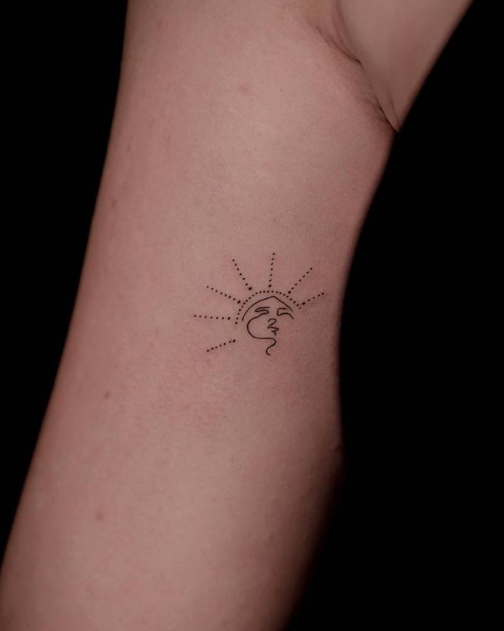 a small sun and moon tattoo on the left side of the arm, which is drawn in black ink