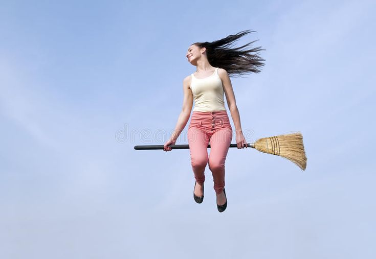 a woman flying through the air on top of a broom and wearing pink pants with her hair blowing in the wind