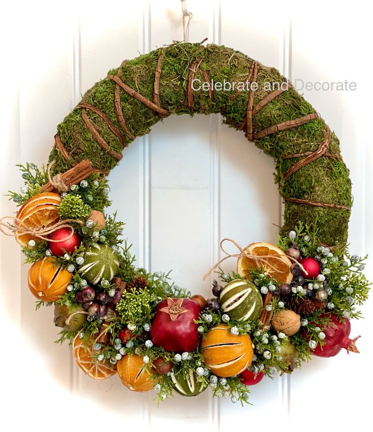 a wreath made out of moss with apples, oranges and other decorations on it