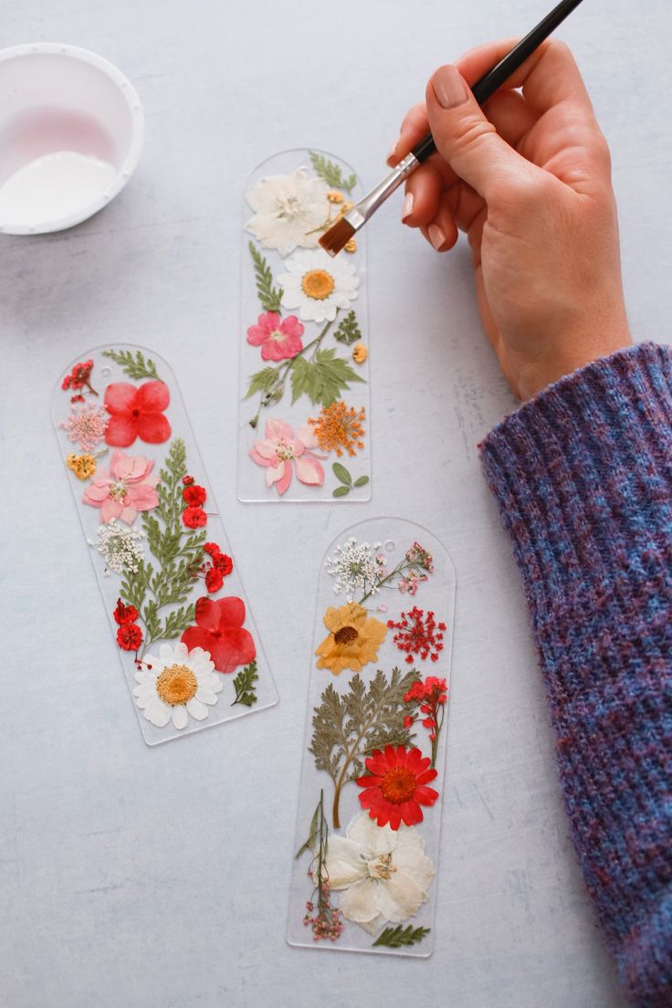 a person is painting flowers on glass tags with paintbrushes and a bowl of milk