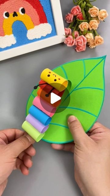 someone is holding a paper toy in front of some flowers and a painting on the wall