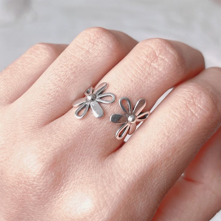 This dainty nature inspired floral ring is entirely made of 925 sterling silver, featured with two daisy flowers. Lovely on its self or stacked with other rings, it is designed to connect your personal expression with self-identity that goes far beyond. Fantastic to give as a gift or to simply treat yourself... ⭐️ ⇩⇩ PRODUCT INFO ⇩⇩ ⭐️ ► Metal: 925 sterling silver with hallmark (nickle free) ► Initial Band Diameter: approx 17.5 mm (UK Size O) ► Open band: adjustable to fit your size ► Hypoallergenic, comfortable to wear ♻️ Eco-Packaging: beautifully wrapped up inside a Kraft box, ready for gift giving! 🌟 GIFTING DIRECT!  FREE GIFT WRAPPING  Just simply mark your order as gift and leave your gift message. No invoices or receipts are included, I will hand write your message within a handmad Delicate Spring Flower Ring, Delicate Flower Shaped Ring For Spring, Dainty Anniversary Rings For Spring, Delicate Toe Flower Ring, Dainty Spring Anniversary Rings, Flower Shaped Anniversary Rings For Spring, Spring Flower Promise Ring, Adjustable Silver Daisy-shaped Jewelry, Adjustable Silver Daisy Jewelry