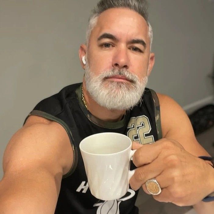 a man with grey hair and beard holding a coffee cup in his hand while looking at the camera