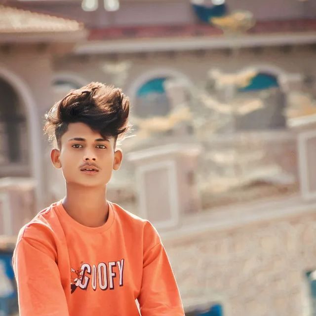 a young boy in an orange shirt is sitting on a skateboard and looking at the camera