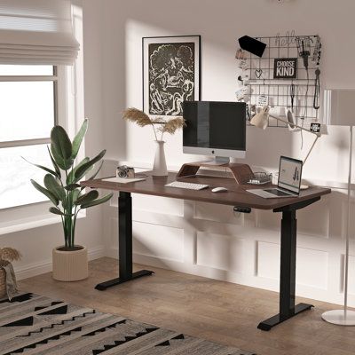 a desk with a computer on top of it in front of a window next to a potted plant