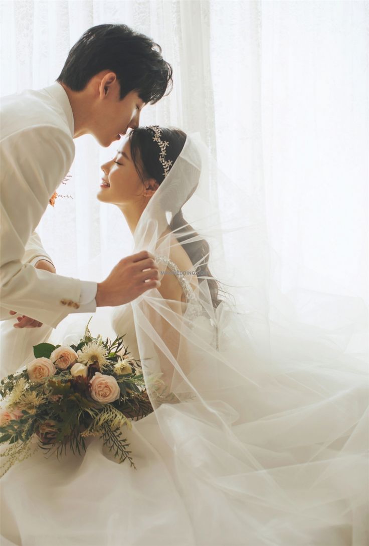 a bride and groom kissing in front of a window