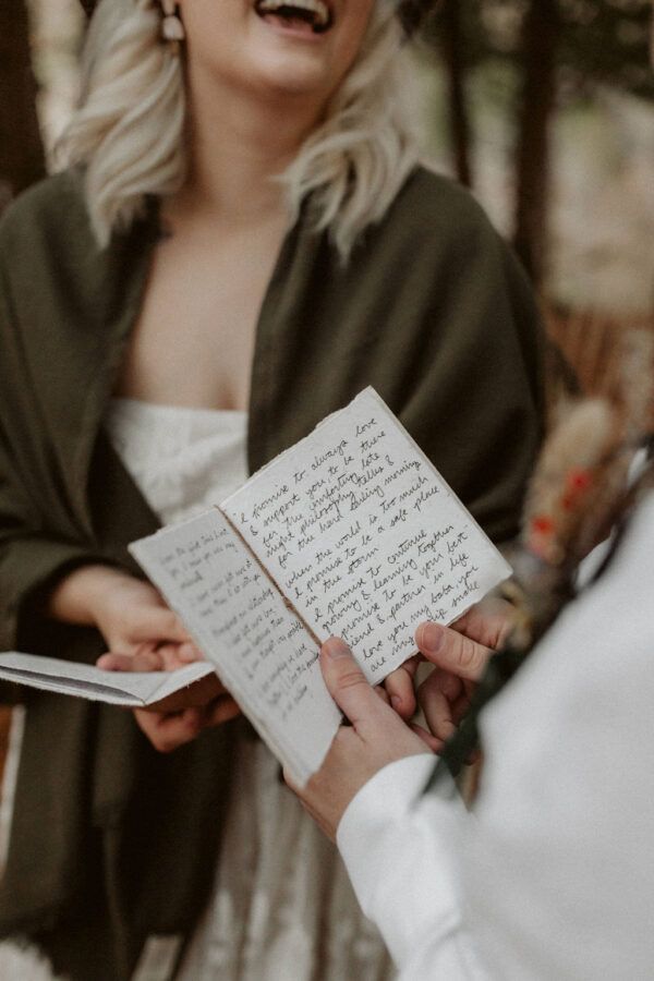 a woman in a white dress holding an open book with writing on it and laughing