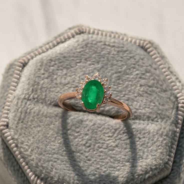 an emerald and diamond ring sitting on top of a cushion