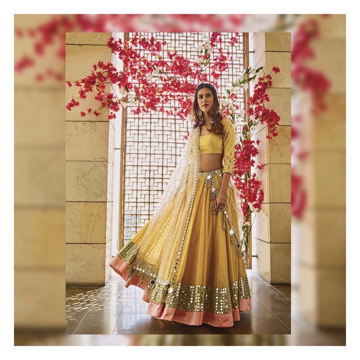 a woman wearing a yellow lehenga and matching with red flowers in the background