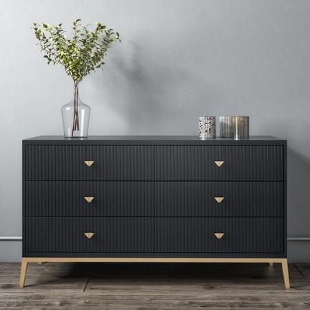 a black dresser with gold handles and drawers in a living room, against a gray wall