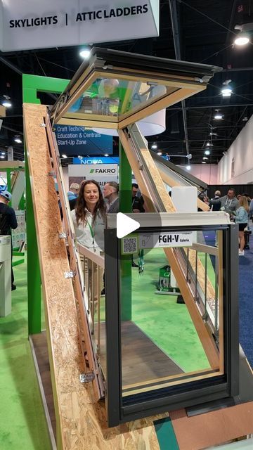 a woman standing in front of a display case at a trade show with people walking around