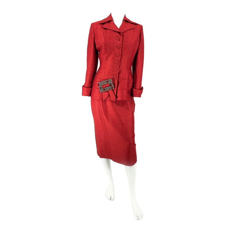 1950s Red Lilli Ann wool and silk blend jacket and skirt suit. The suit jacket features a sharp collar, notch lapel, designer covered buttons, in-set button holes, fitted and tailored wasp waist, and an enlarged clear and red rhinestone buckle attached to an applied swag. The sleeves are finished with rolled and sharp winged cuffs. The body of the jacket is fully lined with a coordinating red textile. The skirt of the suit has an applied and button waist band, back kick-pleat, and a side metal z Elegant Formal Wool Skirt Suit, Elegant Wool Skirt Suit For Formal Occasions, Formal Fitted Single Button Skirt Suit, Fitted Single Button Skirt Suit For Formal, Fitted Single Button Skirt Suit For Formal Occasions, Retro Formal Skirt Suit With Buttons, Classic Evening Skirt Suit With Notch Lapel, Fitted Evening Suits With Button Closure, Evening Fitted Suit With Button Closure