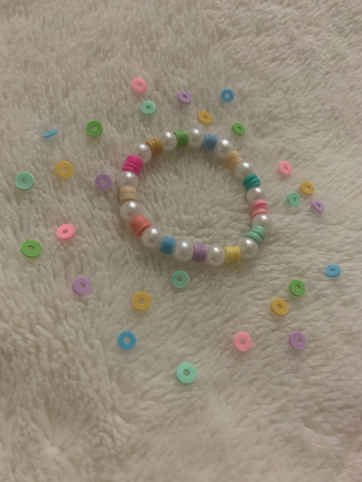 a beaded bracelet with multicolored beads on a white blanket next to a cell phone