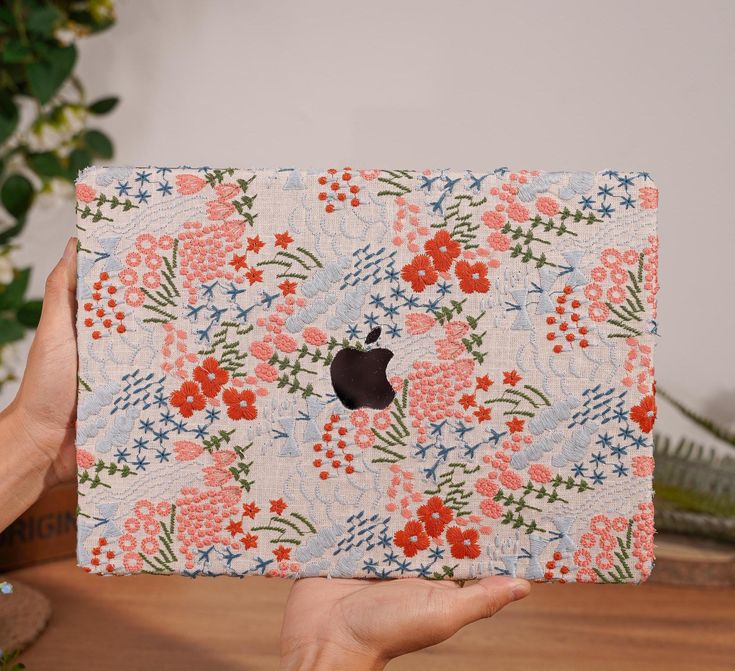 a person holding up an ipad case in front of a potted plant with red and blue flowers on it