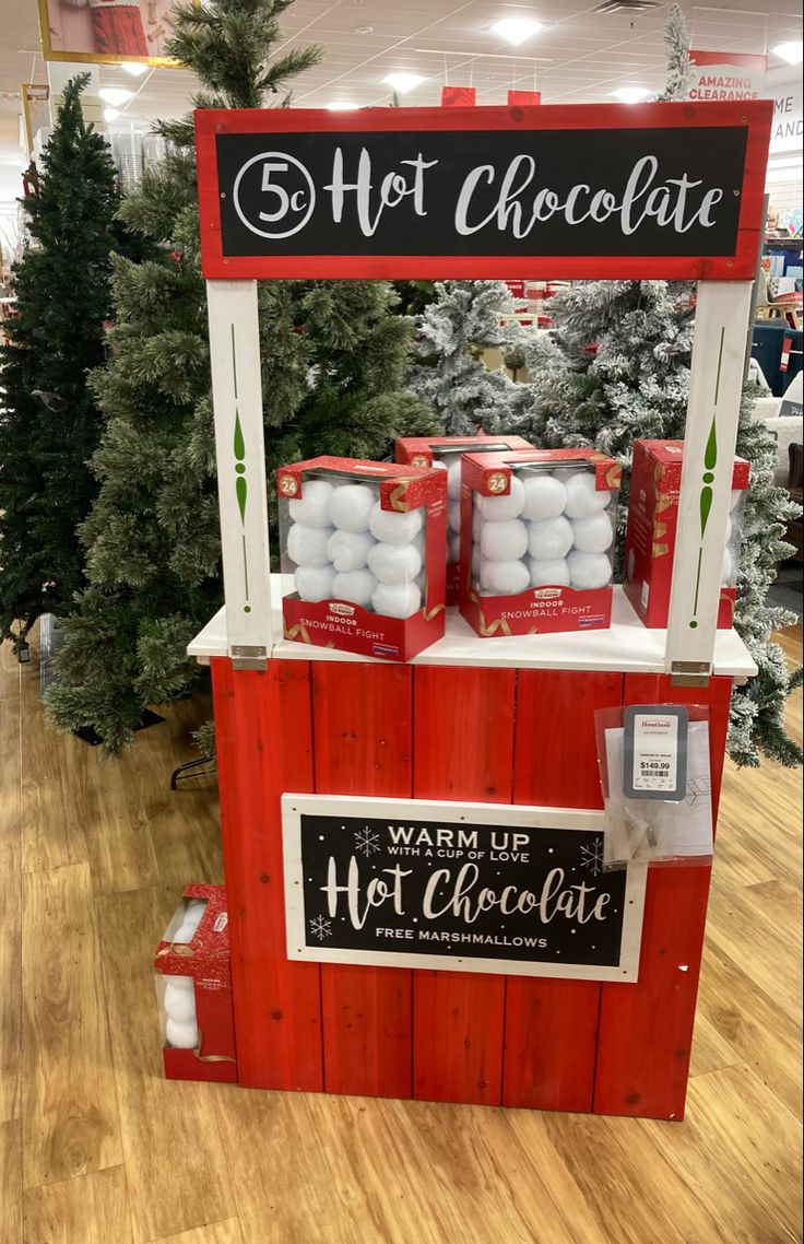 a hot chocolate stand in a store with christmas trees and decorations around the display area