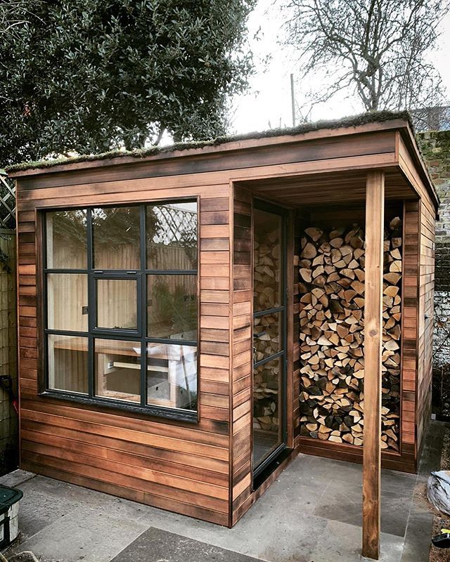 a small wooden shed with wood stacked in it's back door and windows on the side