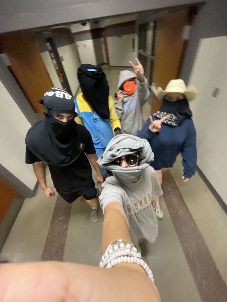 a group of people walking down a hallway with one person wearing a hood and sunglasses