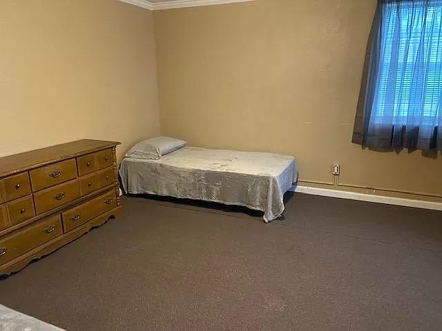 a bedroom with a bed, dresser and window in the corner next to a curtained window