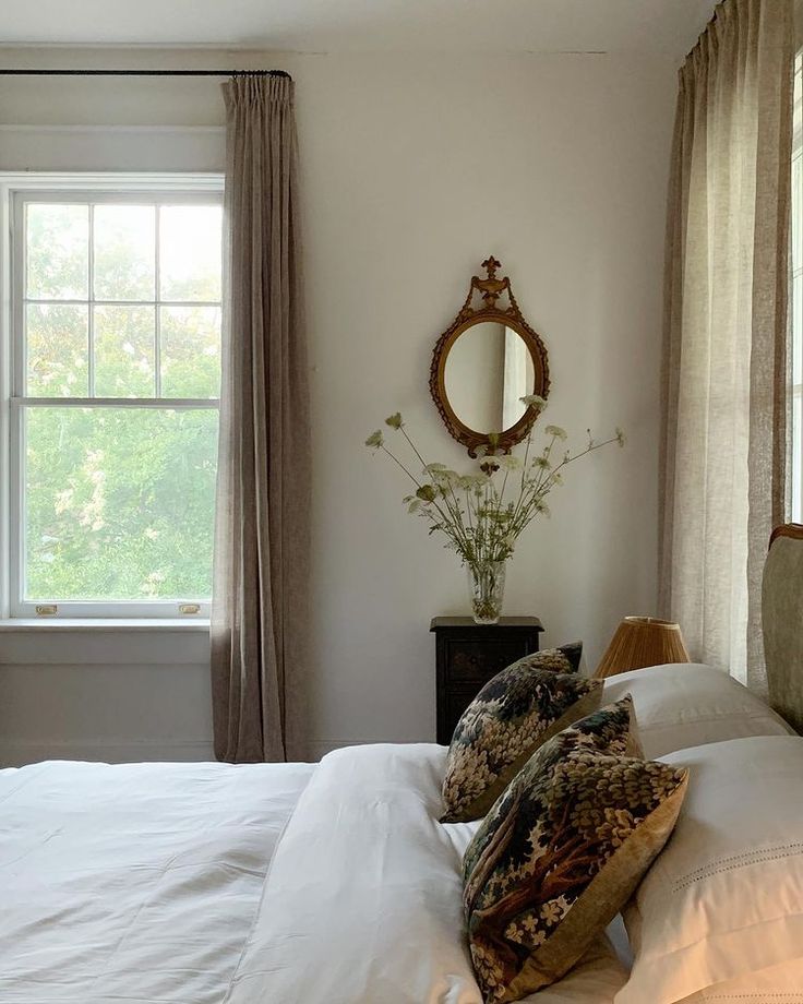 a bed with white sheets and pillows in front of a mirror on the wall above it