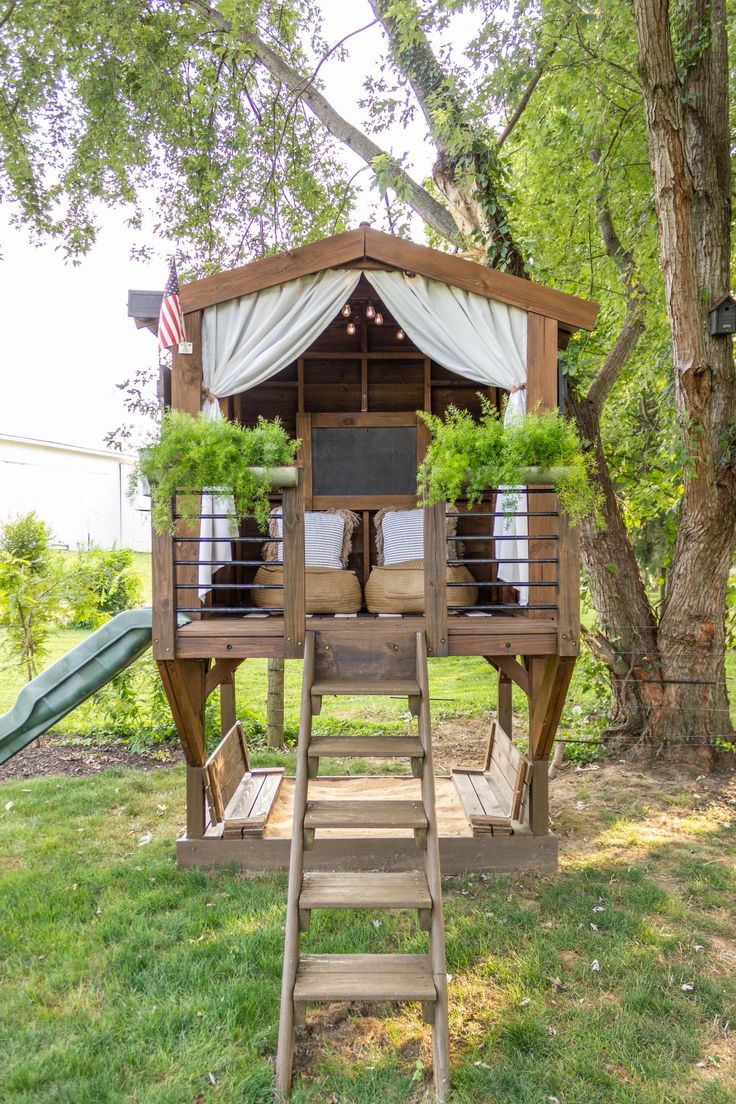 a wooden structure with plants on it in the middle of a grassy area next to a tree