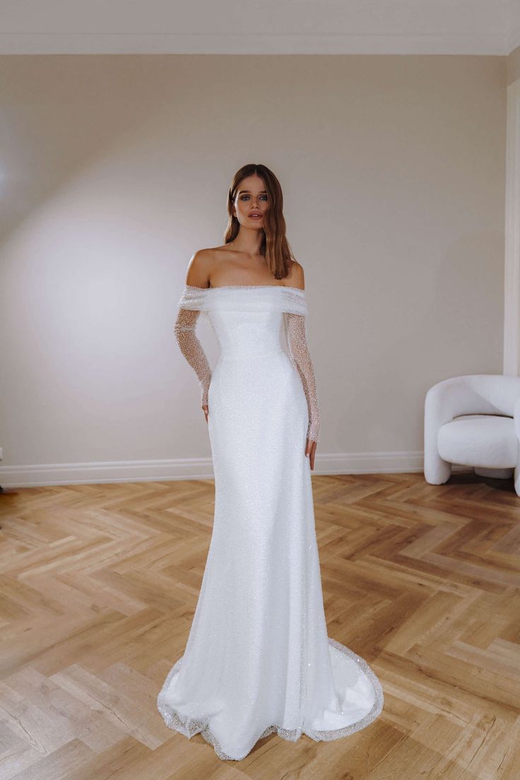 a woman in a white wedding dress standing on a wooden floor with her arms behind her back