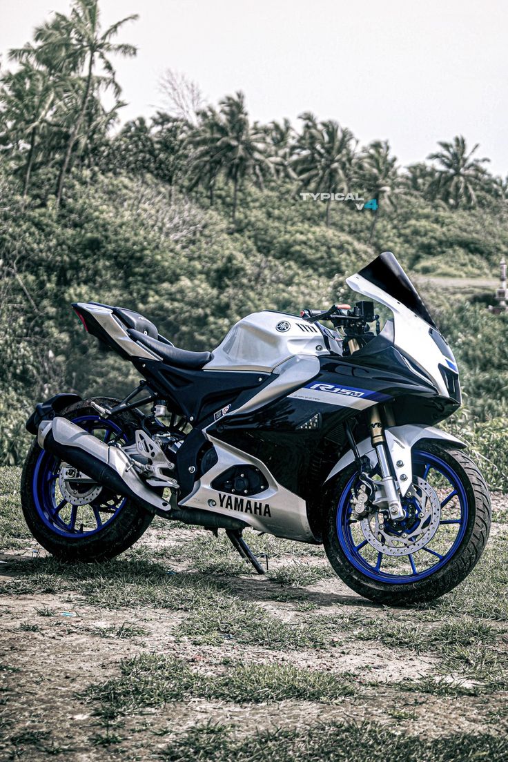 a white and blue motorcycle parked on top of a grass covered field next to trees