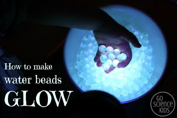 a person holding their hand over a bowl filled with water beads that glow in the dark