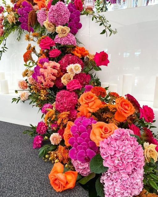 an arrangement of colorful flowers on display in front of a white wall and black carpet