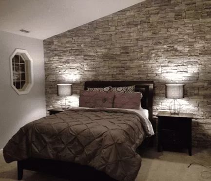 a bedroom with a bed and two lamps on either side of the headboard, in front of a stone wall