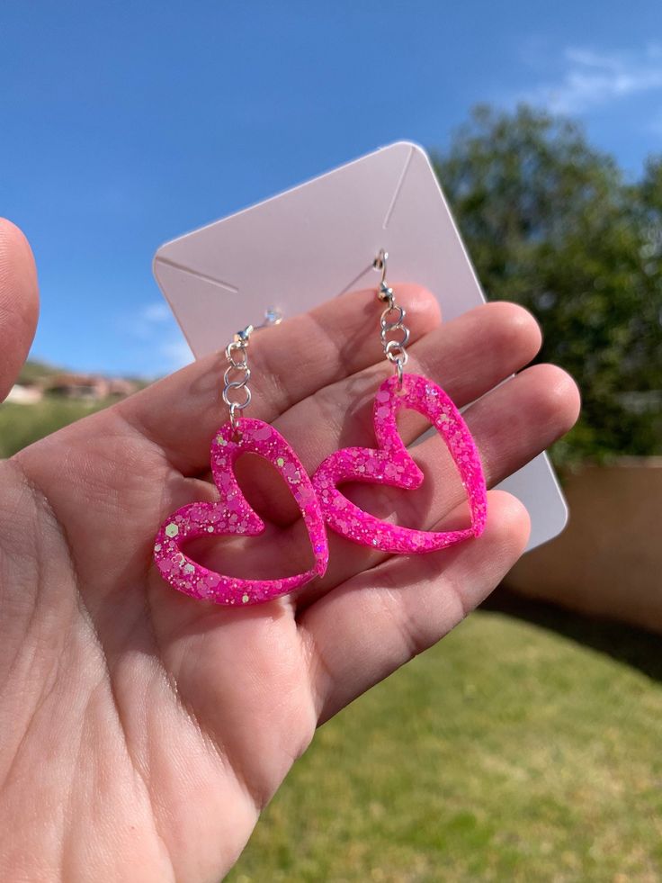 Each pair of glittery pink resin heart earrings are handmade to order, therefore no two pairs are identical! However, I try to get as close as possible :) Made with nickel free, hypoallergenic, sterling silver plated fishhooks.  Heart is approximately 3cm x 3cm and is made with epoxy resin and neon hot pink iridescent mix glitter  💖 Please note that the hearts will hang at an angle. Thanks for visiting my shop! ✨ Cute Pink Glitter Earrings, Pink Resin Heart Earrings For Gift, Pink Resin Heart Earrings As Gift, Pink Heart Resin Earrings, Pink Glitter Heart Earrings For Party, Cute Glitter Jewelry Gift, Cute Resin Heart Earrings For Valentine's Day, Cute Pink Resin Jewelry, Pink Glitter Earrings For Valentine's Day