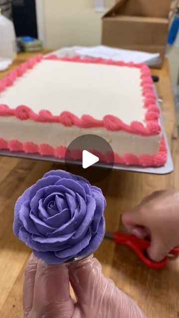 a person is cutting a cake with purple icing and a rose on top that has been decorated