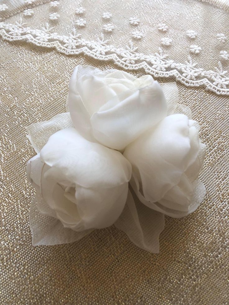 three white flowers sitting on top of a lace covered table cloth next to a doily