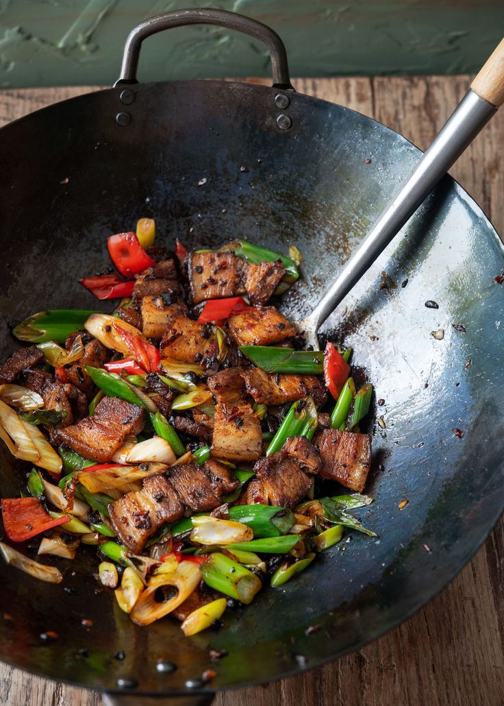 a wok filled with meat and vegetables on top of a wooden table