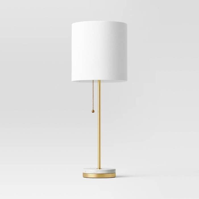 a white lamp with a gold base and a white shade on the top is shown