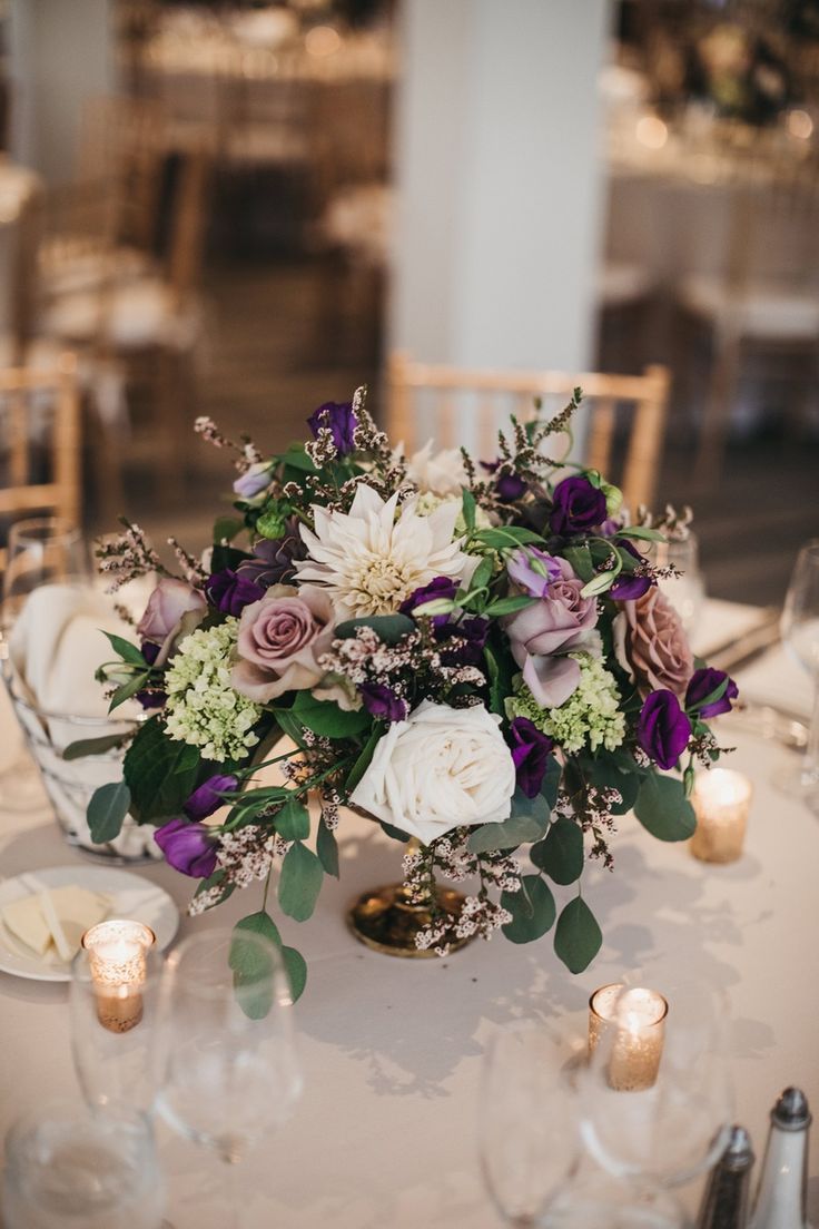 the centerpieces on this table are filled with purple and white flowers, greenery, and candles