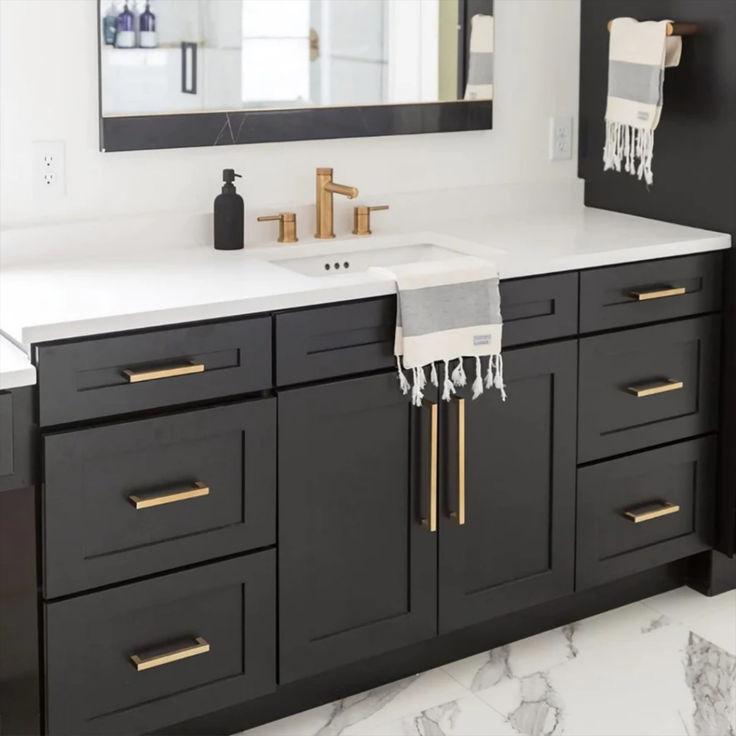 a bathroom with black cabinets and white counter tops, gold hardware on the faucet