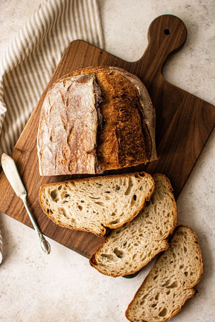 a loaf of bread sitting on top of a cutting board next to slices of bread