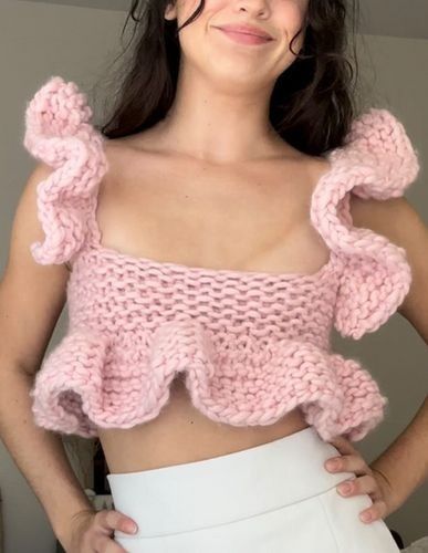 a woman wearing a pink knitted top with ruffles on the shoulders and bottom