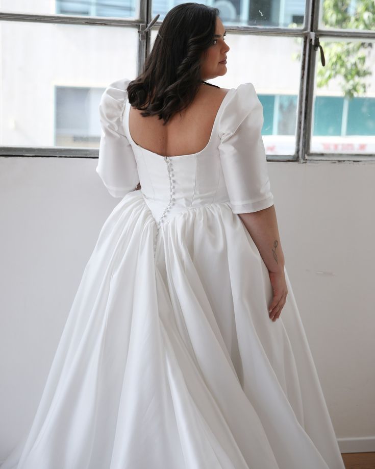 a woman in a white wedding dress looking out the window with her back to the camera