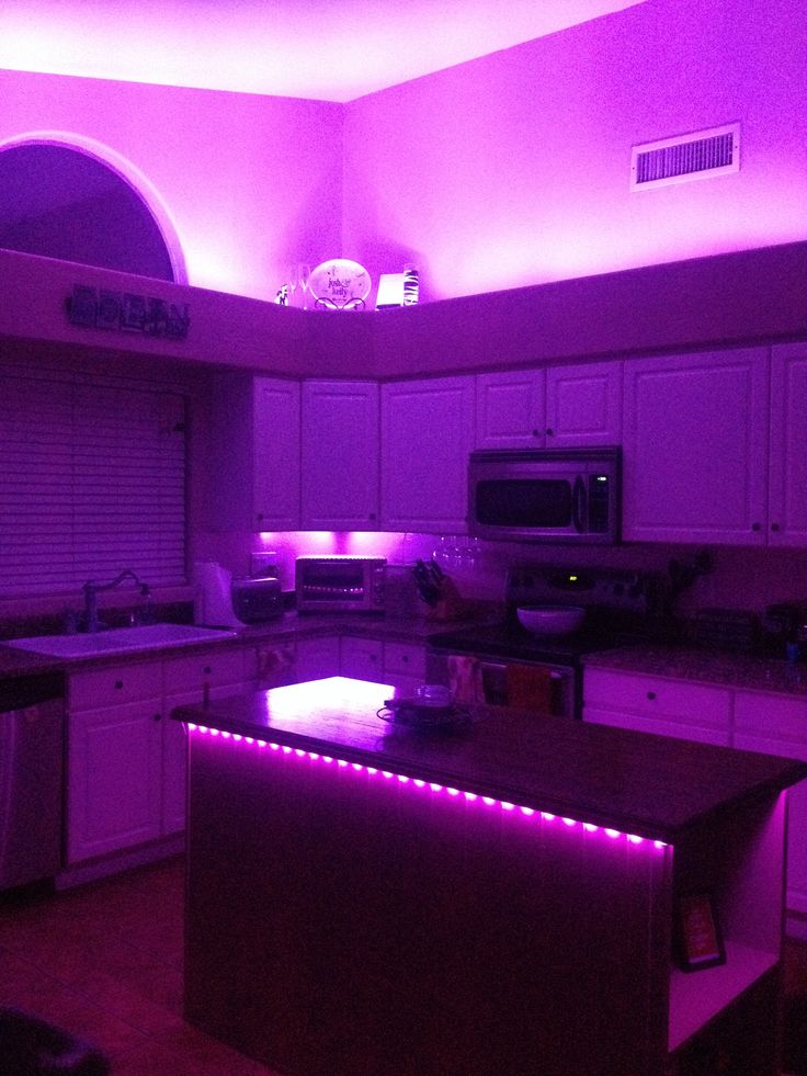 a kitchen with purple lights on the ceiling and counter tops in front of an oven