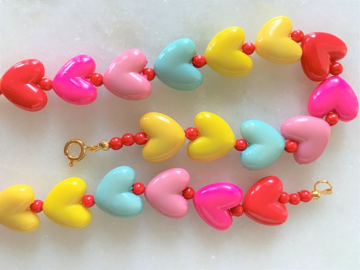 "Kids Brite Multi Colored Plastic Heart Necklace with Red Mini Spacer Beads Gold Tone Spring Ring Clasp Closure Brite Multi Hearts are Red, Hot Pink, Pink, Aqua, Yellow Hearts Measure 5/8\" Wide Necklace Measures 15\" Imported COMPLIMENTARY DOMESTIC SHIPPING" Playful Jewelry With Heart Beads, Adjustable Double Heart Necklace With Heart Beads, Fun Heart Beads Jewelry As Gift, Playful Heart Beads Jewelry, Cute Multicolor Beaded Necklaces With Heart Beads, Adjustable Heart Beaded Necklaces, Playful Heart Jewelry For Valentine's Day, Mother's Day Adjustable Heart Beads Necklace, Playful Adjustable Beaded Necklaces With Heart Beads