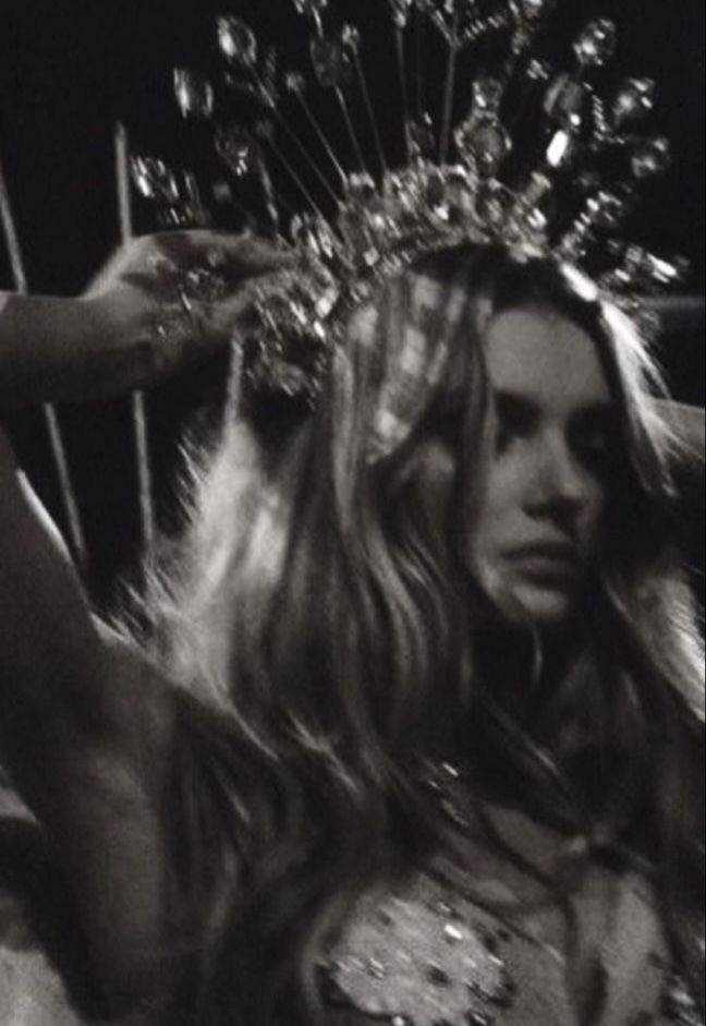 a woman with long hair and a crown on her head standing in front of a mirror