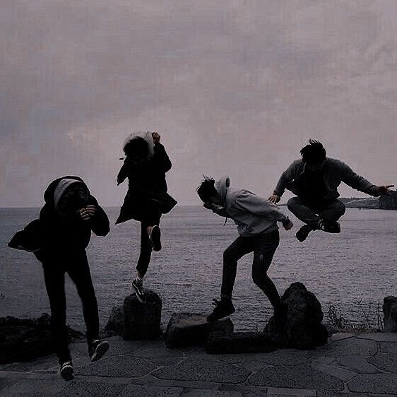 three skateboarders jumping off rocks into the water on a cloudy day in black and white