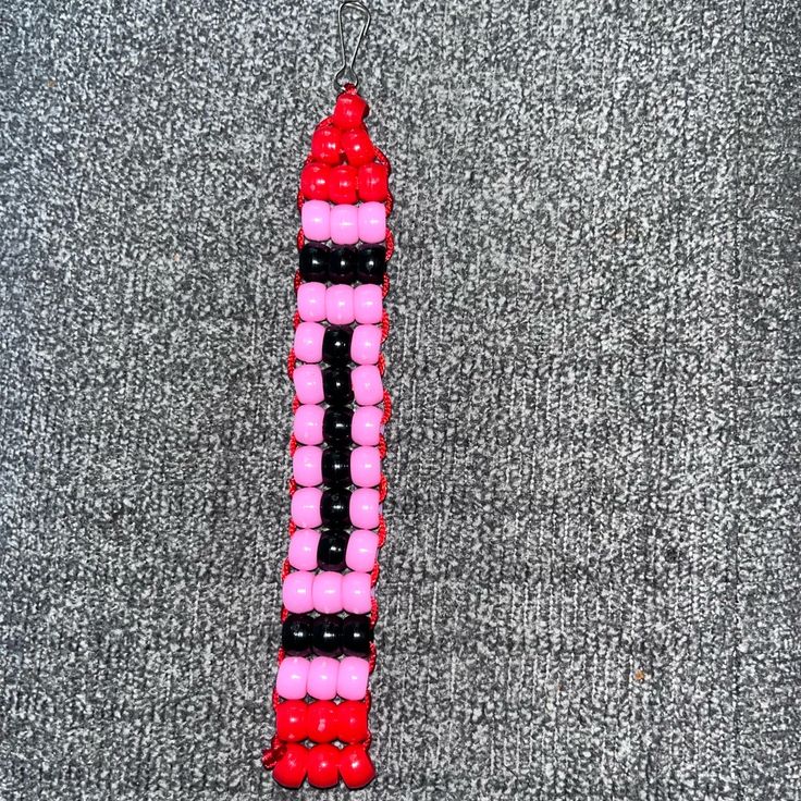 a pink, black and white beaded object laying on top of a gray carpet